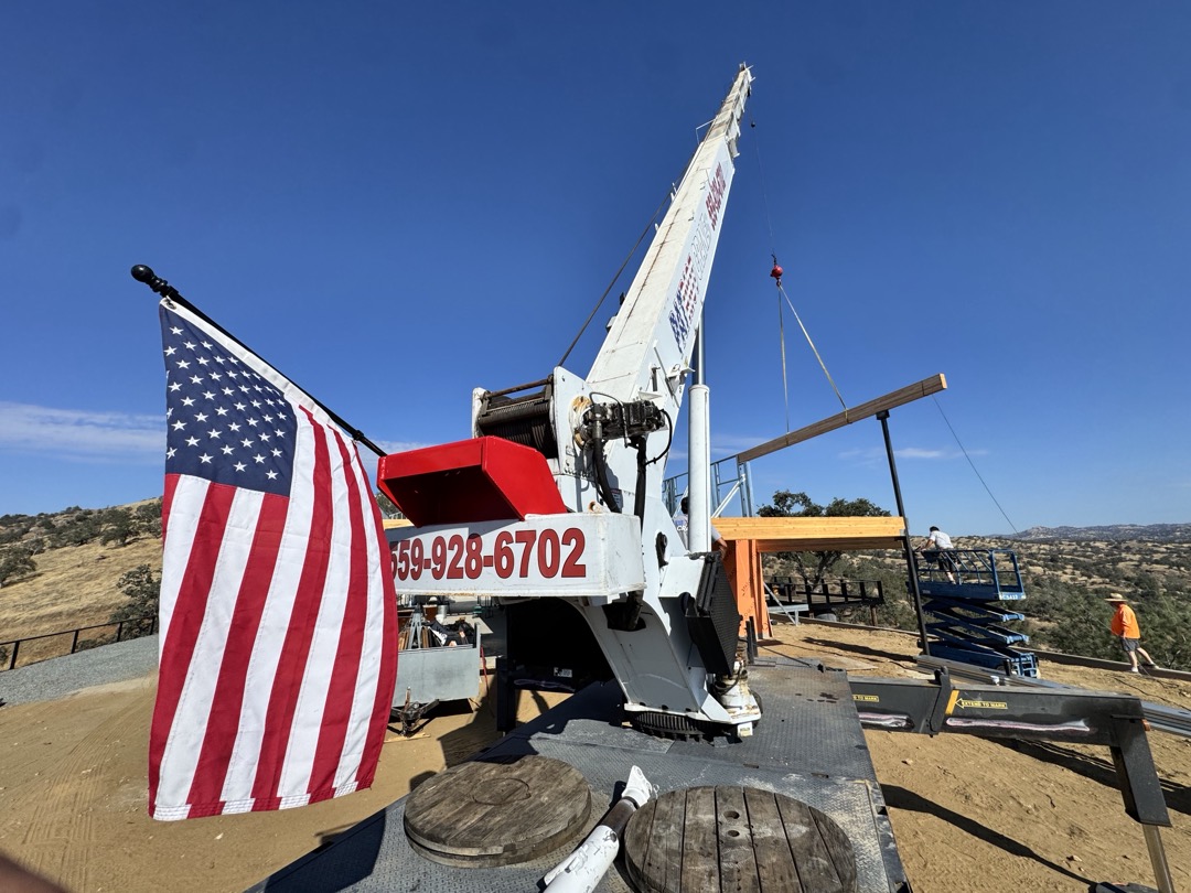 Patriot Crane lifting a beam on a Fresno-area hilltop build, American flag on the rig, 559-928-6702